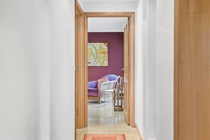 A hallway leading to a room with a purple sofa and a white chair. - Barber`s Hyde | 2BR, Walk to Cafés & Waterfront (Lindisfarne)