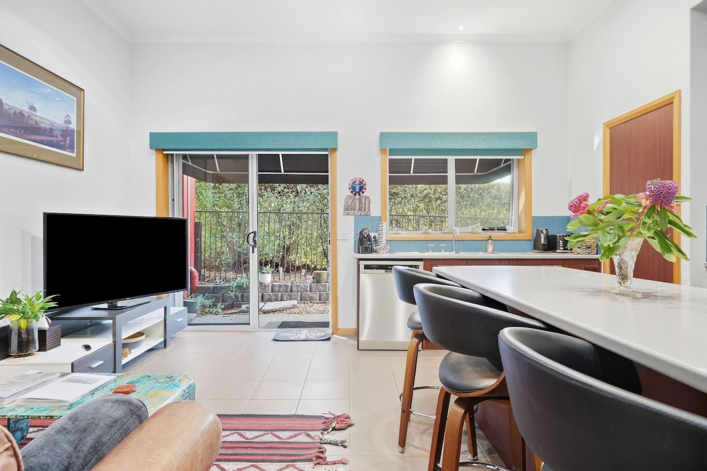 A modern kitchen with a dining area, a flat-screen TV, and a view of the outdoors.