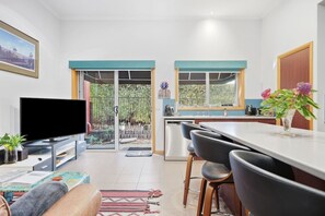 A modern kitchen with a dining area, a flat-screen TV, and a view of the outdoors. - Barber`s Hyde | 2BR, Walk to Cafés & Waterfront (Lindisfarne)