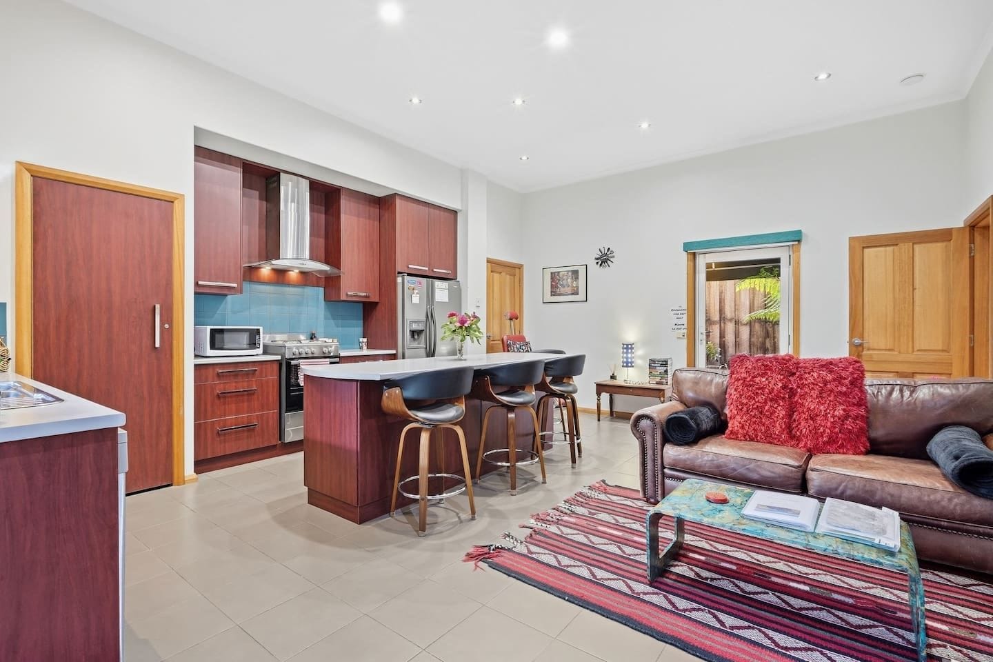 A modern kitchen with a central island, bar stools, a dining table, and a leather sofa.