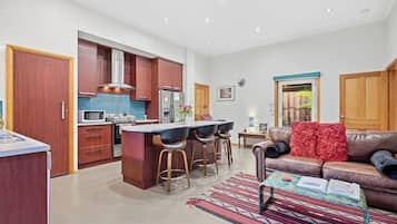 A modern kitchen with a central island, bar stools, a dining table, and a leather sofa.