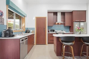 A modern kitchen with a central island, built-in appliances, and bar stools. - Barber`s Hyde | 2BR, Walk to Cafés & Waterfront (Lindisfarne)