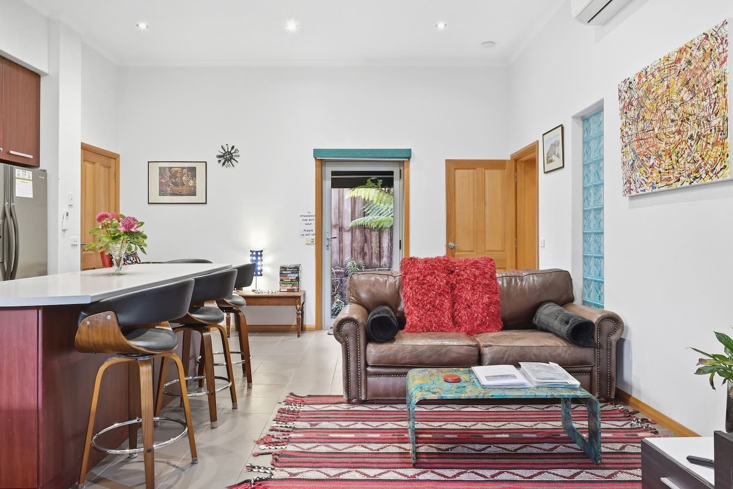 A modern living room with a brown leather sofa, a coffee table, and a dining area with a bar stool.