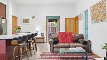 A modern living room with a brown leather sofa, a coffee table, and a dining area with a bar stool.