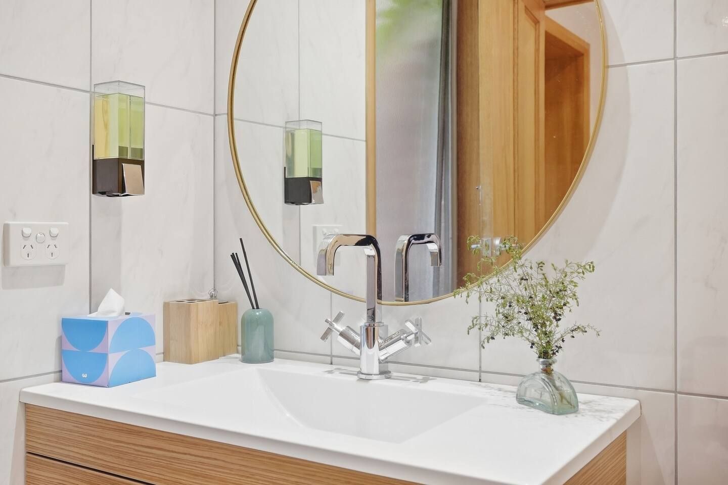 A bathroom with a white sink, a round mirror, and a wooden door.