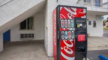 A Coca-Cola vending machine with a selection of beverages, located outside a building with an office sign.
