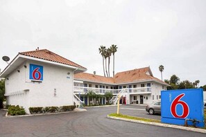 A motel with a prominent '6' sign, a parking lot, and a building with a red-tiled roof.