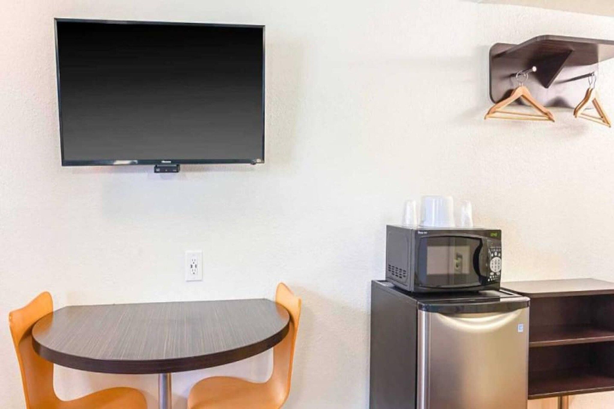 A compact kitchenette with a microwave, a small refrigerator, and a flat-screen TV mounted on the wall.