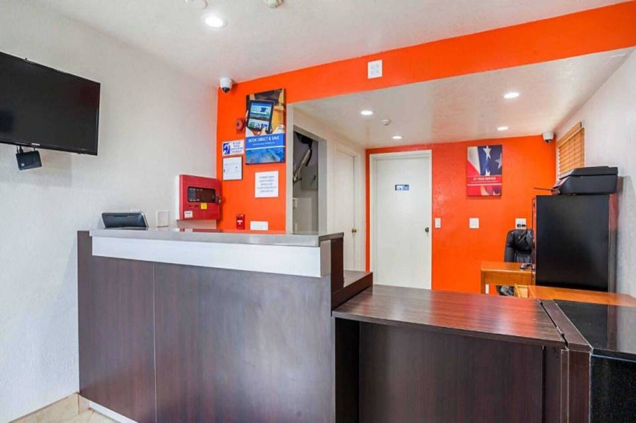 A reception area with a counter, a television mounted on the wall, and a door leading to another room.