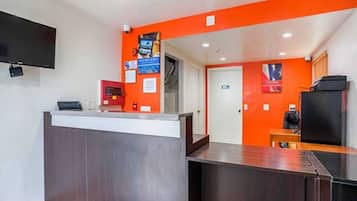 A reception area with a counter, a television mounted on the wall, and a door leading to another room.