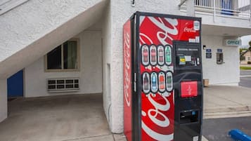 A Coca-Cola vending machine with a selection of beverages, located outside a building with an office sign.