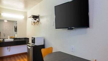 A compact kitchen with a microwave, toaster, and sink. A flat-screen TV is mounted on the wall above a dining table with two chairs.