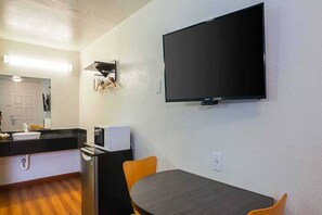 Una cocina funcional con microondas, tostadora y lavabo. Un televisor de pantalla plana está montado en la pared sobre una mesa de comedor con dos sillas.