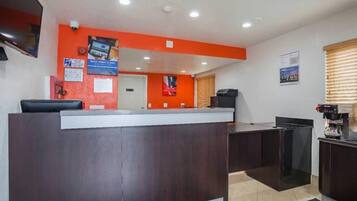 A reception desk with a dark wood finish, a flat-screen TV mounted above it, and a window with blinds to the right.