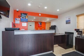 A reception desk with a dark wood finish, a flat-screen TV mounted above it, and a window with blinds to the right. - 1 King Bed | Non-Smoking, Micfridge (Ventura)