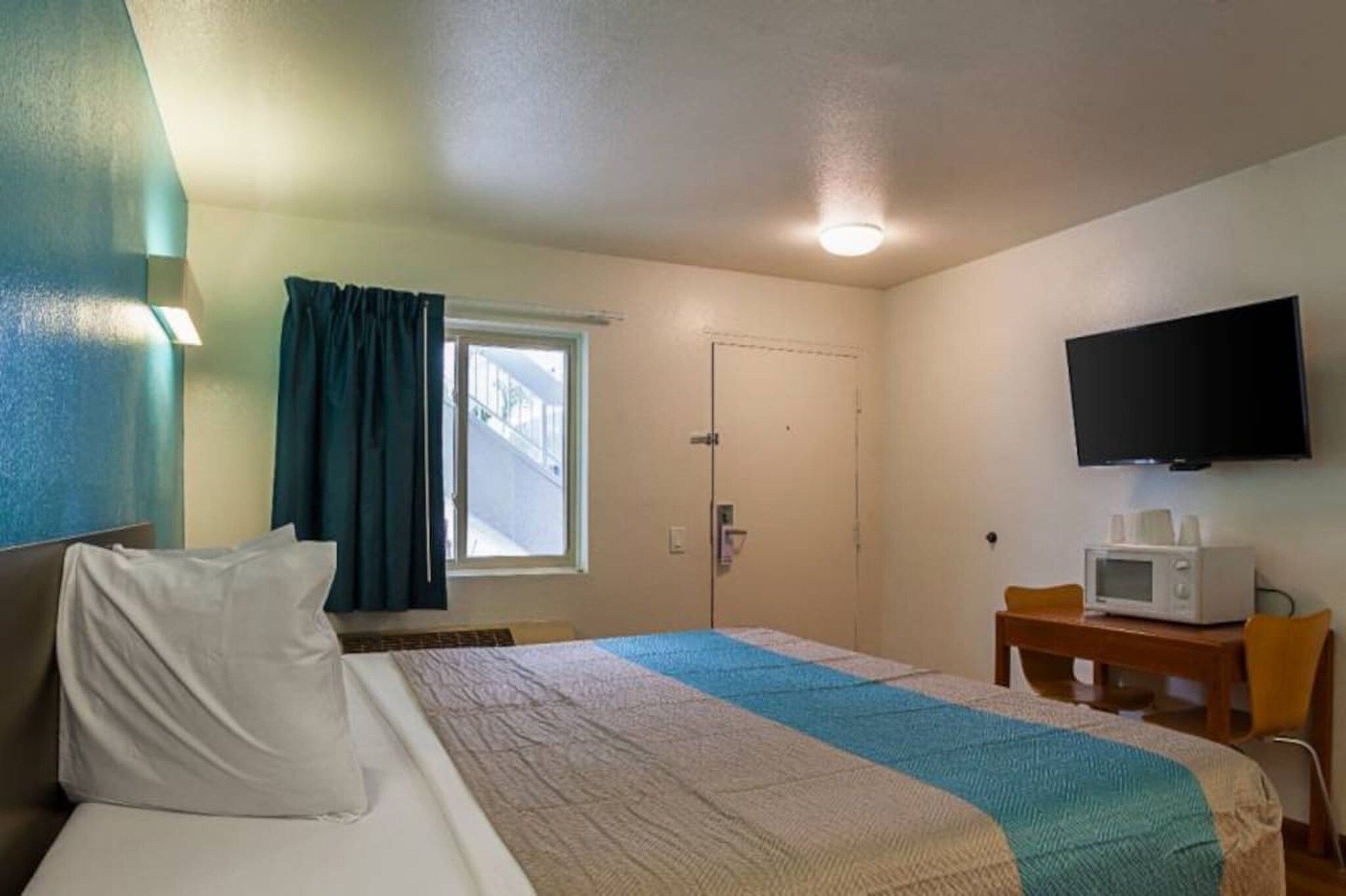 A hotel room with a bed, a television, a microwave, and a window with curtains.