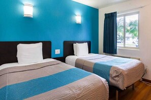 Een hotelkamer met twee bedden, een raam met gordijnen en uitzicht op het omliggende landschap.