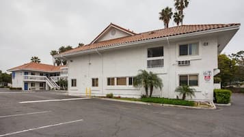 A two-story building with a flat roof, multiple windows, and a parking lot in front.