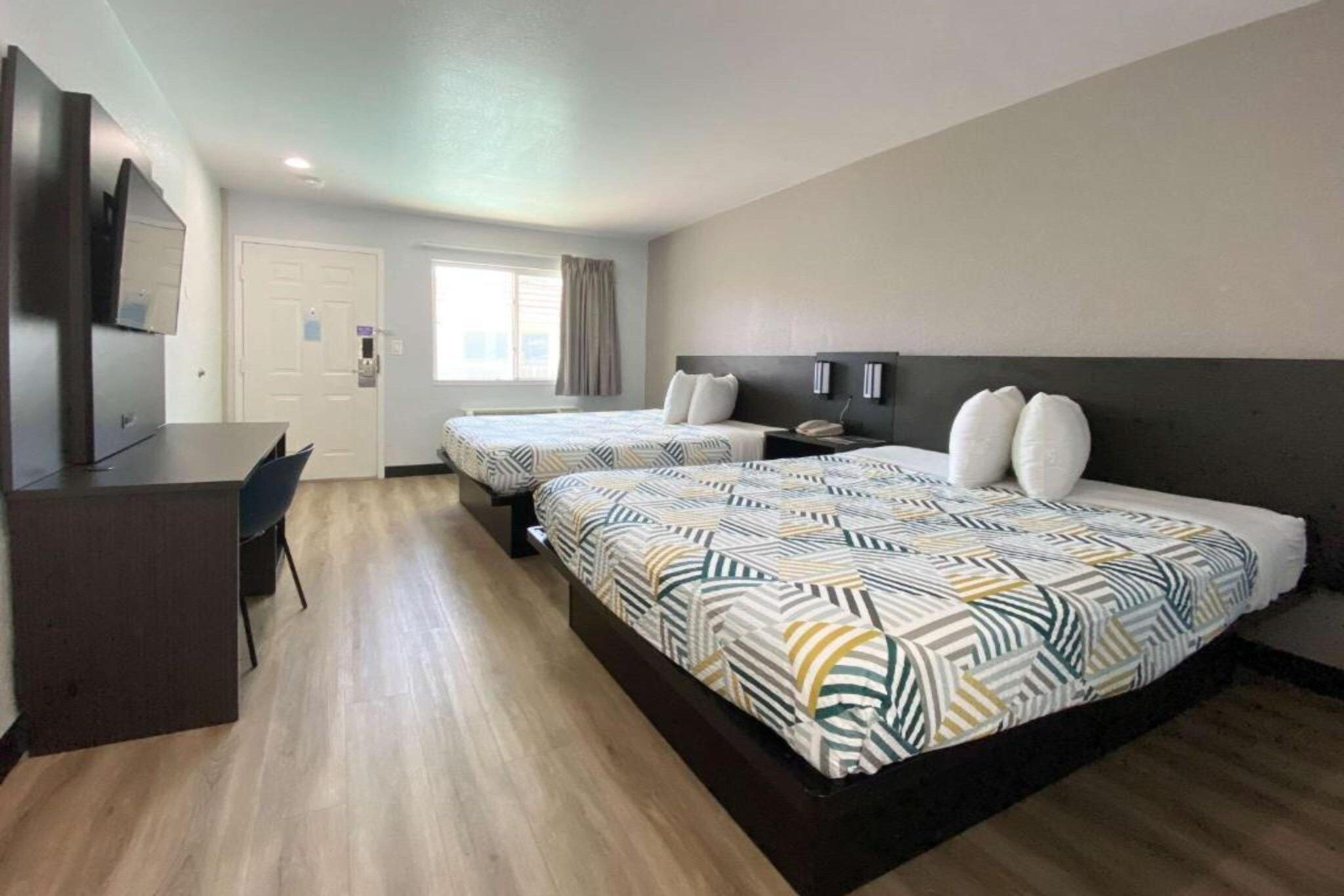 A hotel room with two beds, a desk, and a TV.