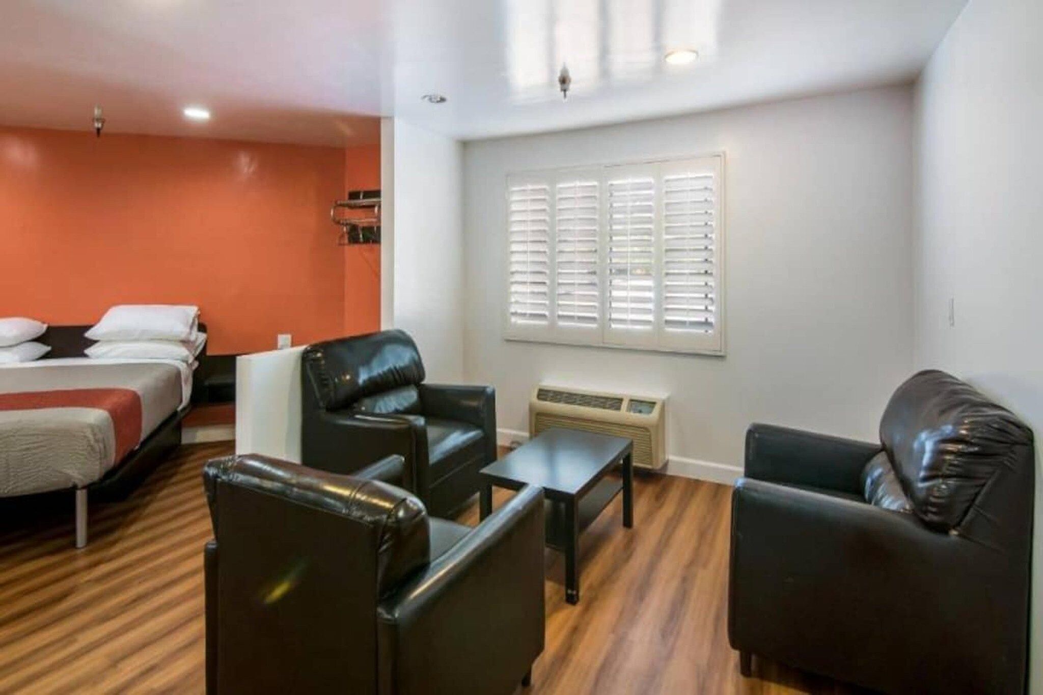 A hotel room with a bed, two black leather chairs, a small table, and a window with blinds.