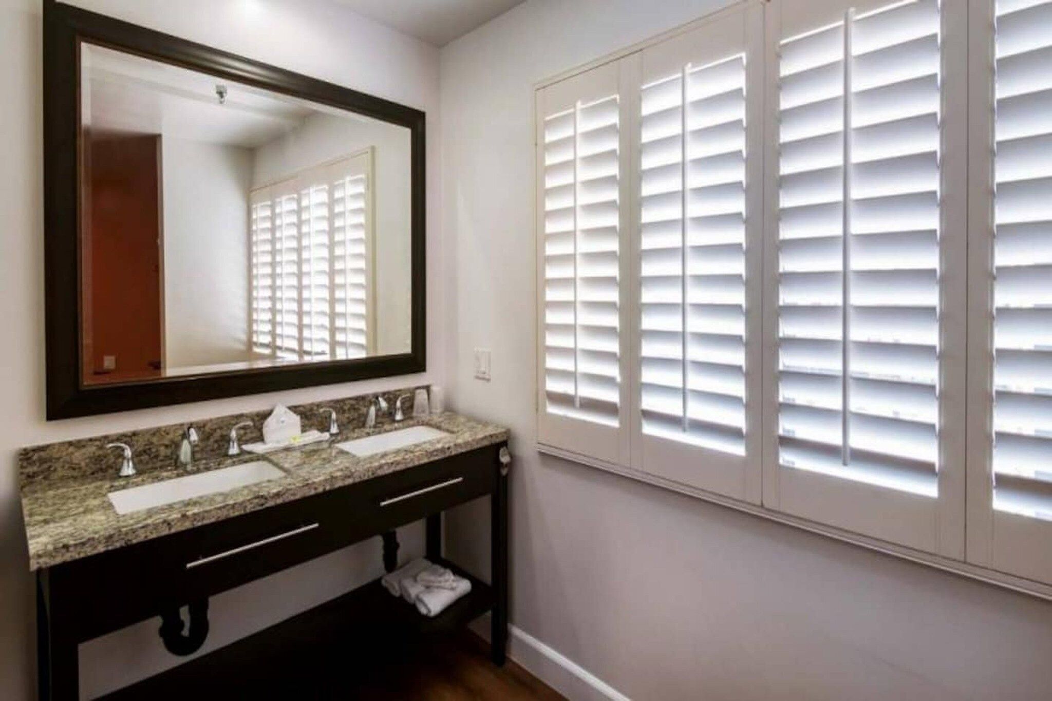 A bathroom with a double sink vanity, a large mirror, and a window with blinds.