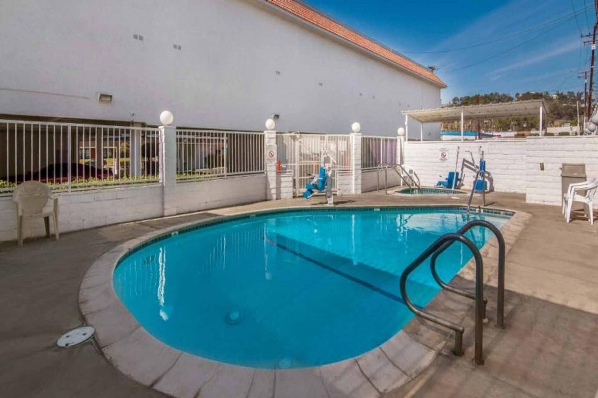 A swimming pool with a metal ladder, surrounded by a white fence with light fixtures.