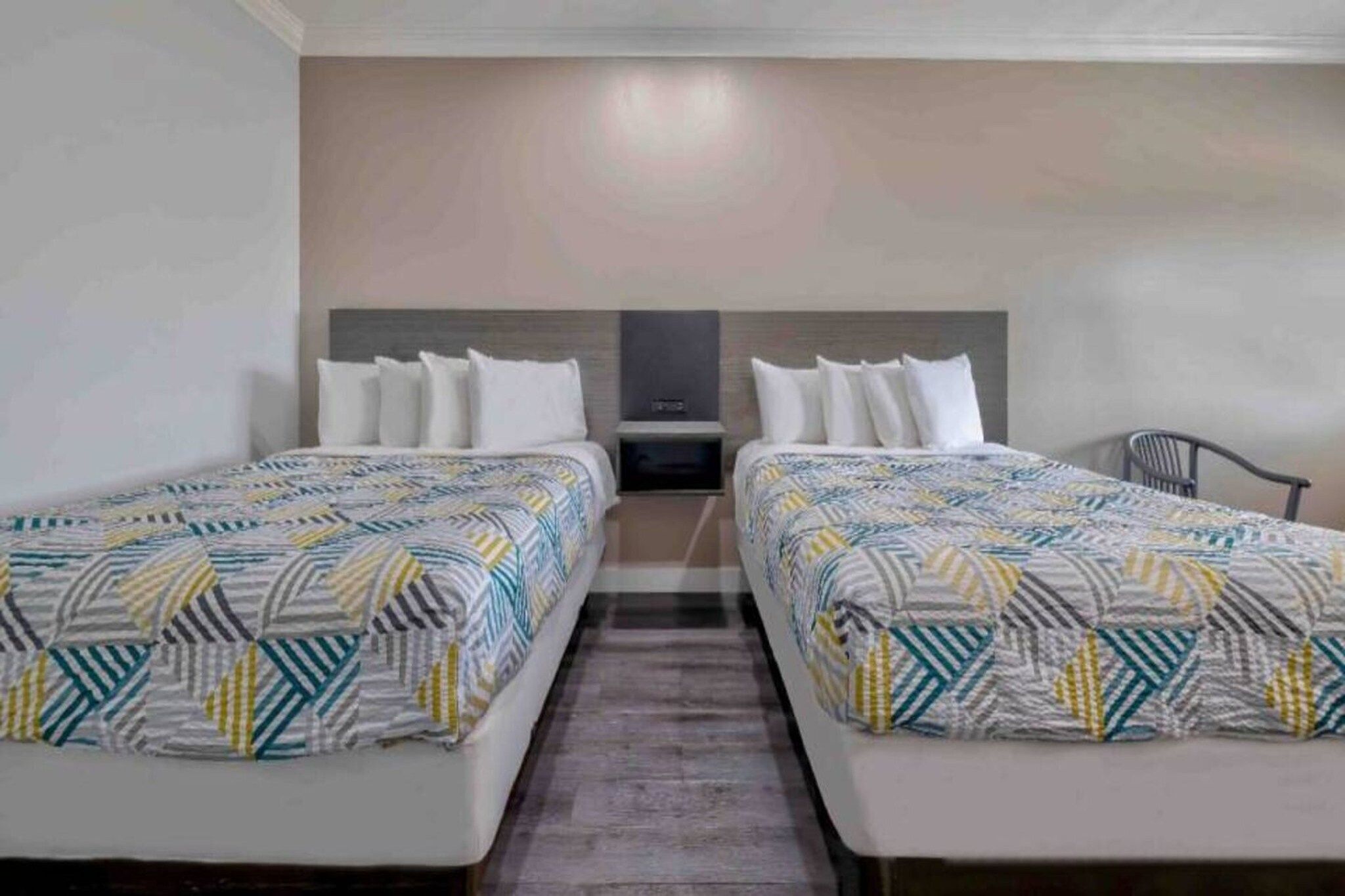 A hotel room with two beds, a nightstand, and a chair.