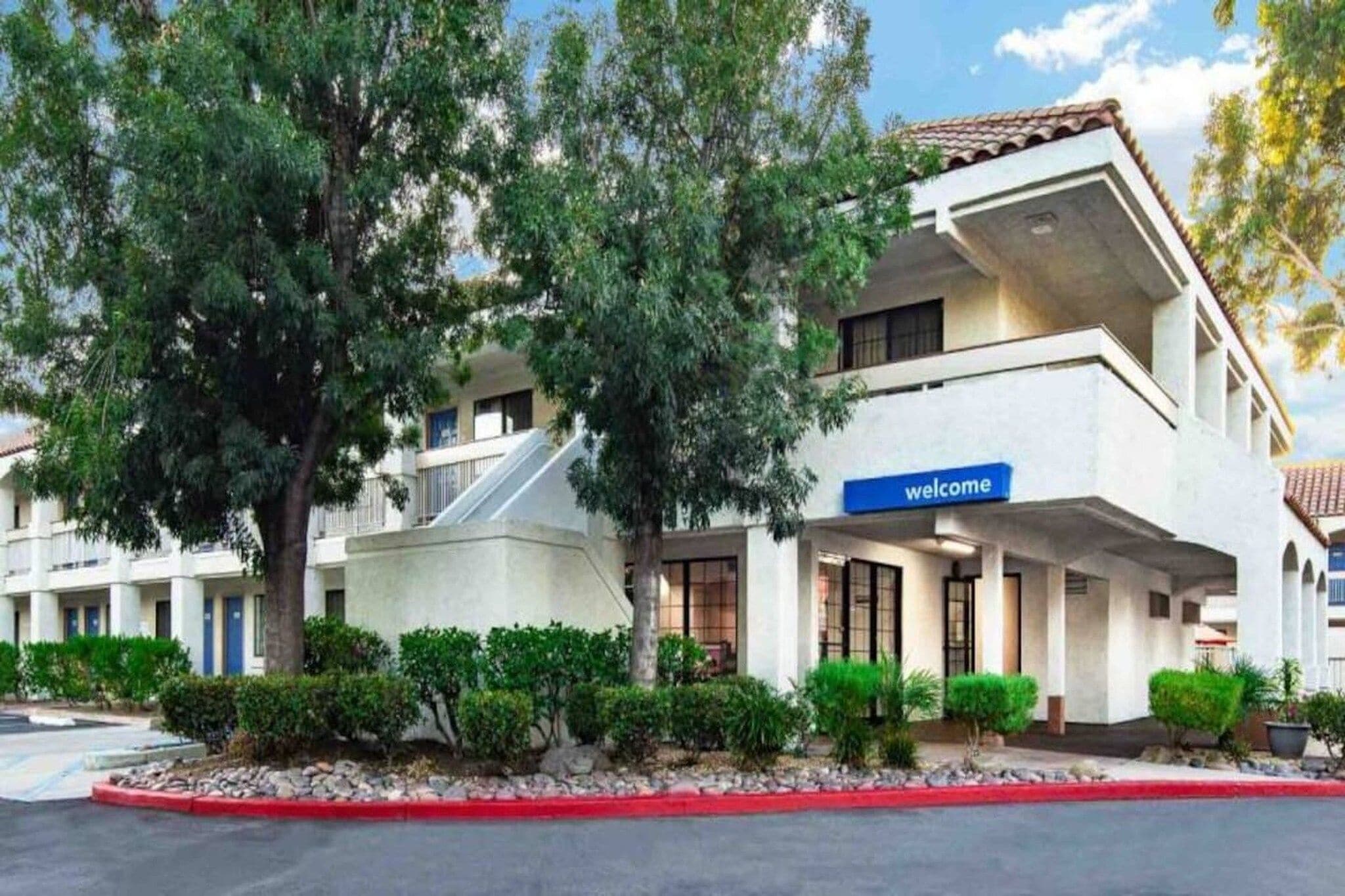 A multi-story hotel with a 'welcome' sign, outdoor seating, and a red curb.