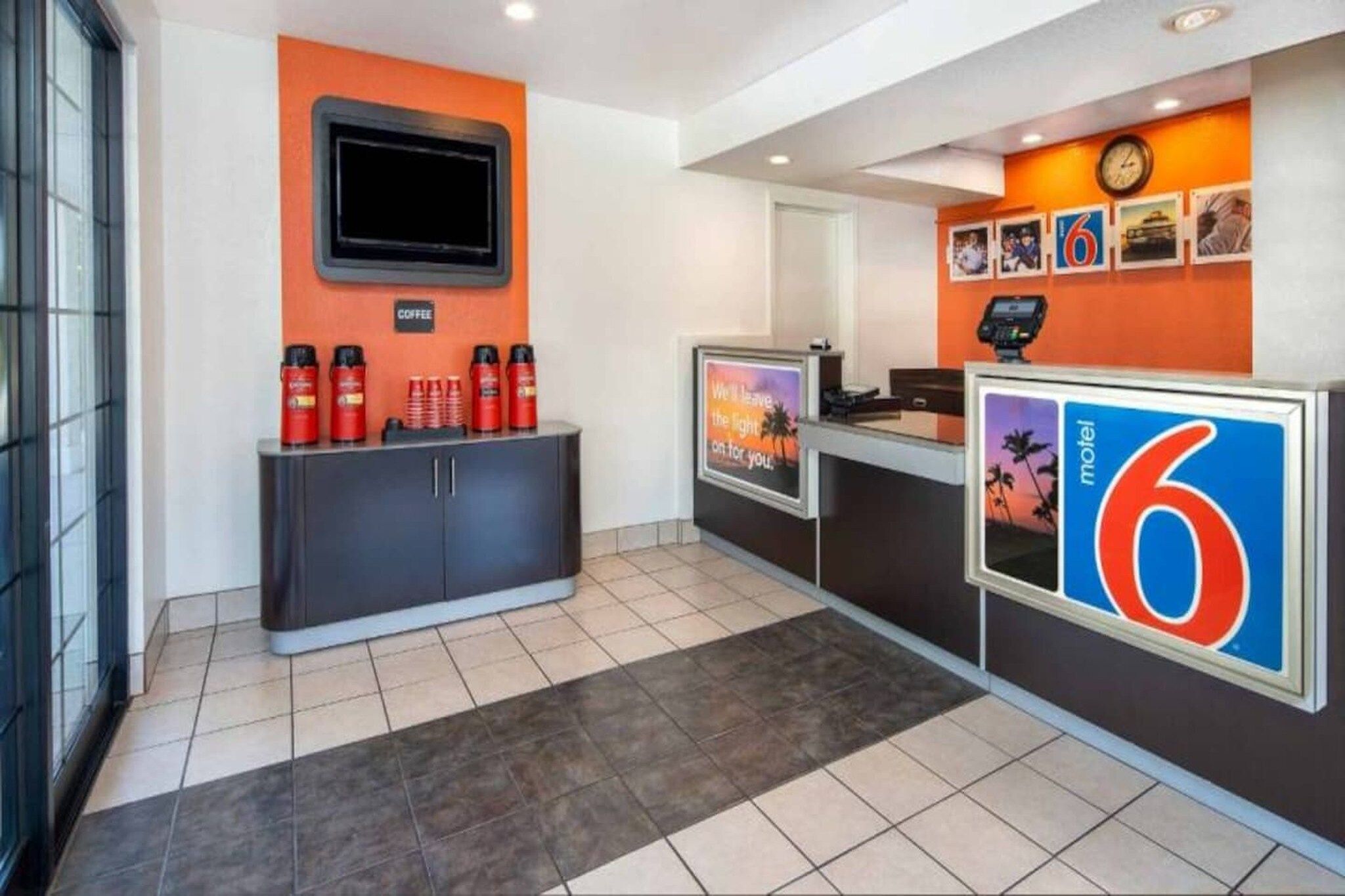 A hotel reception area with a counter, a coffee station, and a digital display.