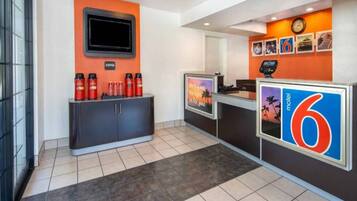 A hotel reception area with a counter, a coffee station, and a digital display.