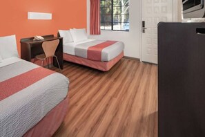 Una camera d'albergo con due letti, una scrivania, una sedia e una finestra con tende.