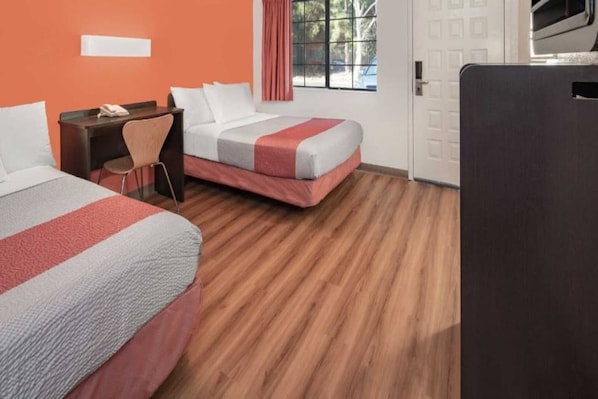 A hotel room with two beds, a desk, a chair, and a window with curtains.