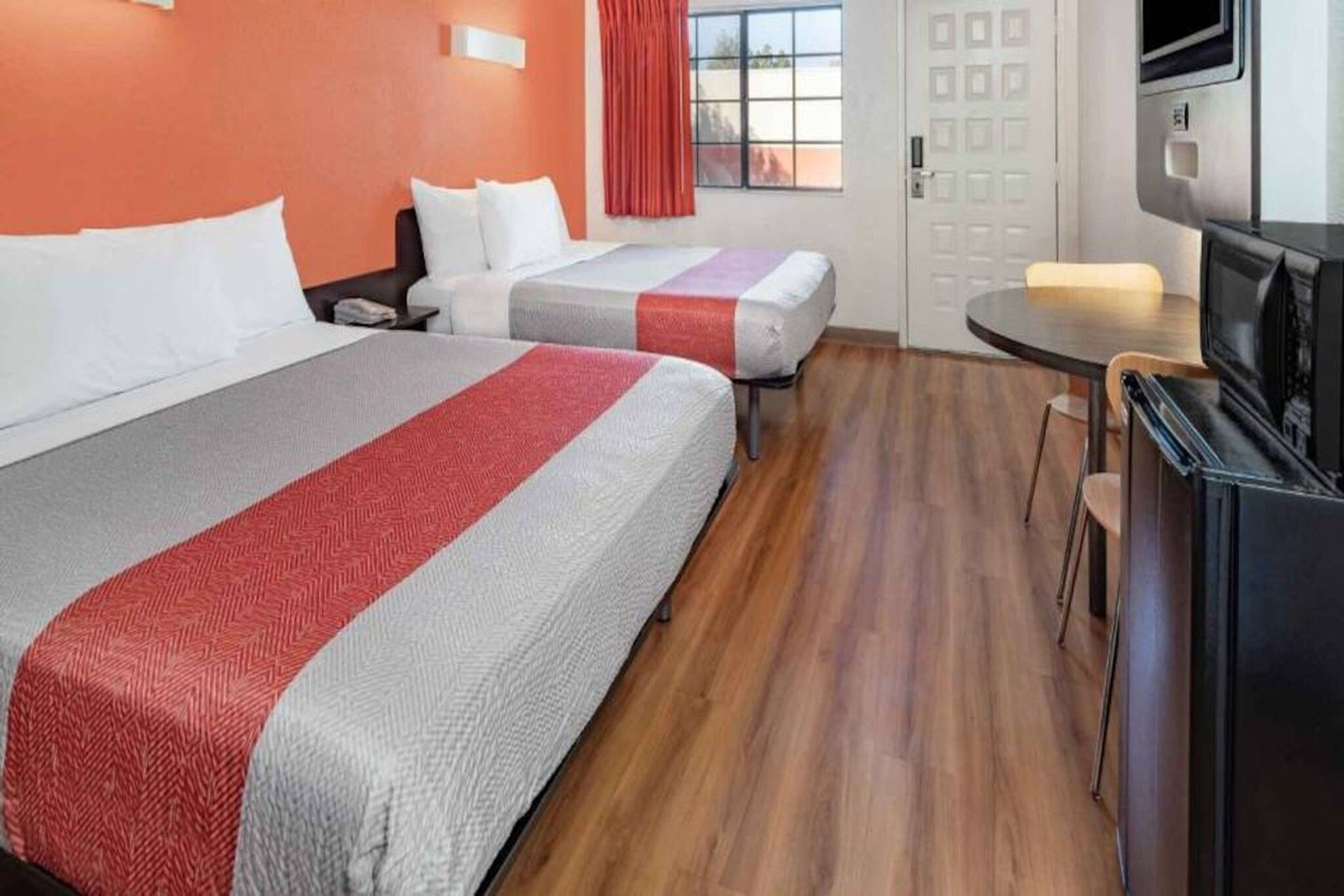 A hotel room with two beds, a small table, a TV, and a window with curtains.