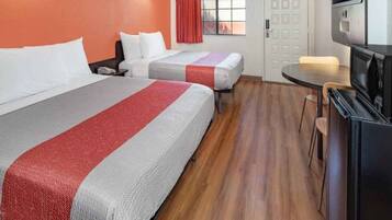A hotel room with two beds, a small table, a TV, and a window with curtains.