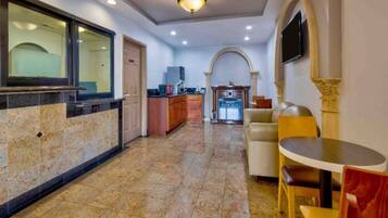 A hotel lobby with a reception desk, a kitchen area, and seating arrangements.