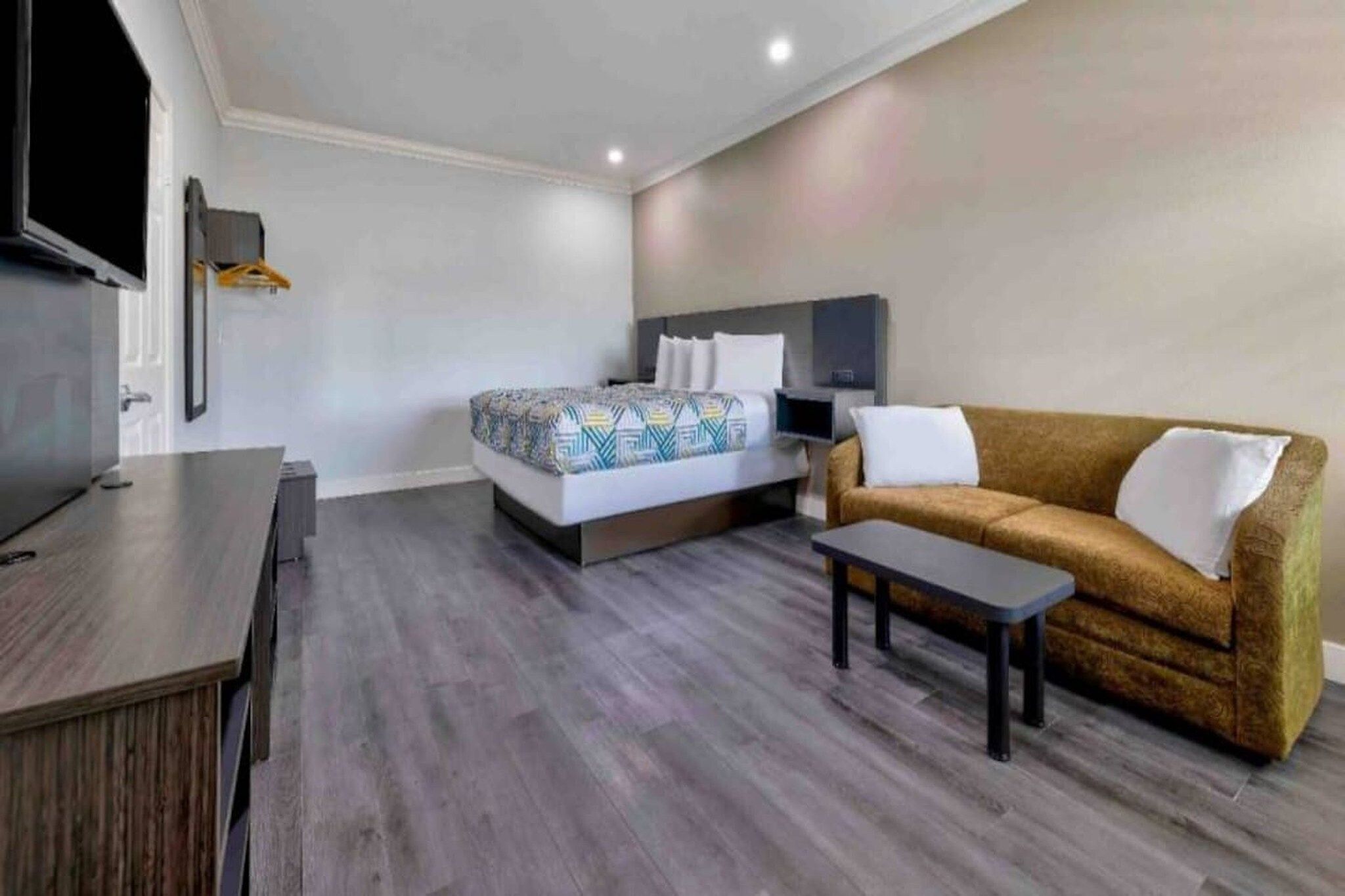 Una camera d'albergo moderna con un letto, una poltrona, una TV e una scrivania.