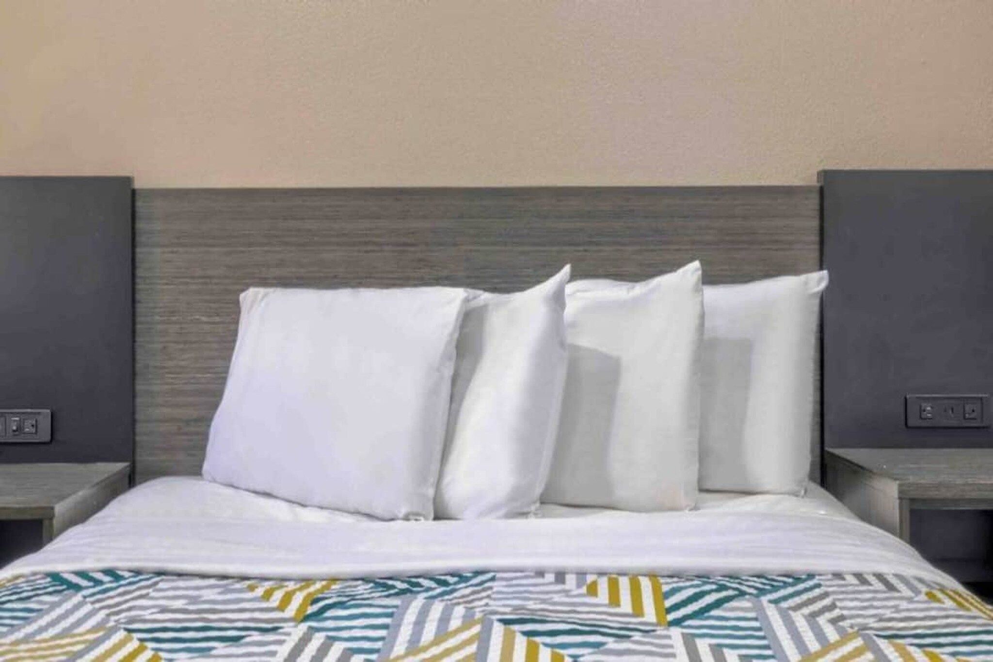 A hotel room with a bed, white pillows, a patterned bedspread, and two bedside tables with controls.