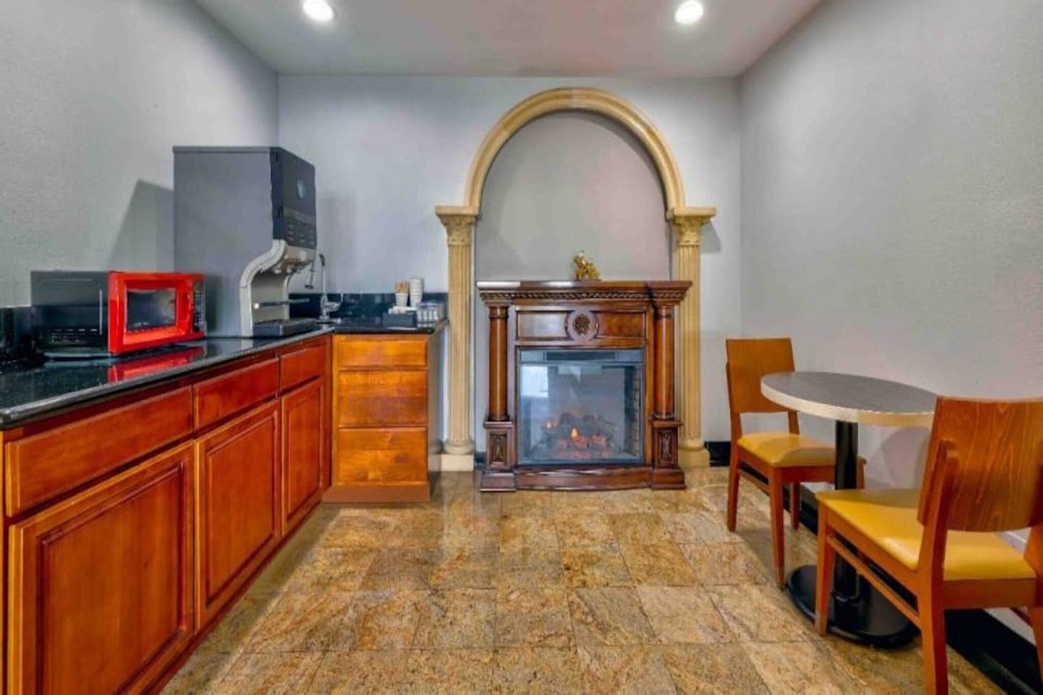 Una cocina con armarios de madera, microondas, cafetera, chimenea y una mesa de comedor con sillas.