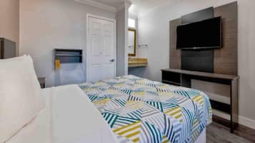 A hotel room with a bed, a television mounted on the wall, and a door.