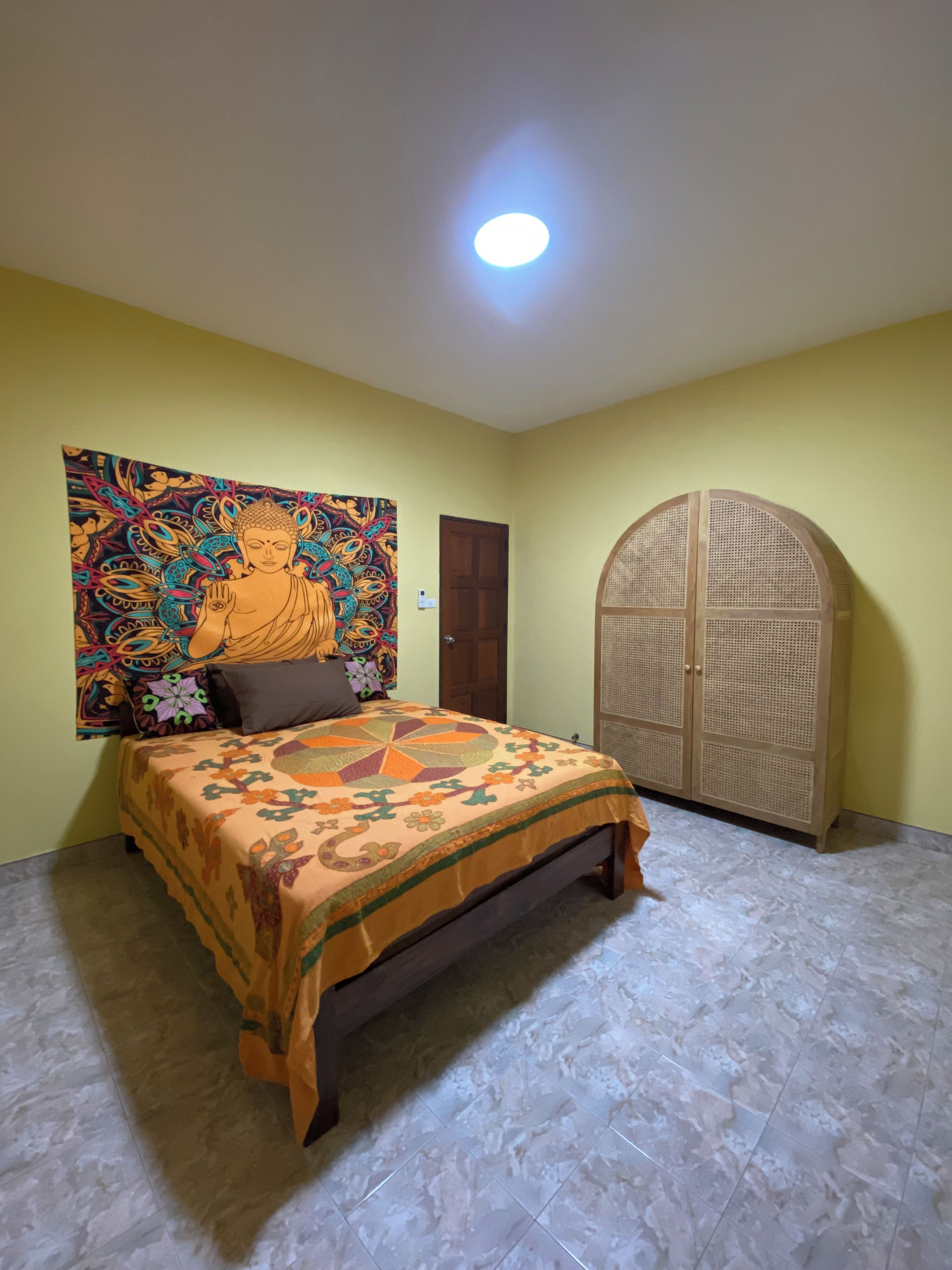 A room with a bed, a door, and a wall with a colorful tapestry.