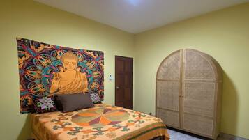 A room with a bed, a door, and a wall with a colorful tapestry.