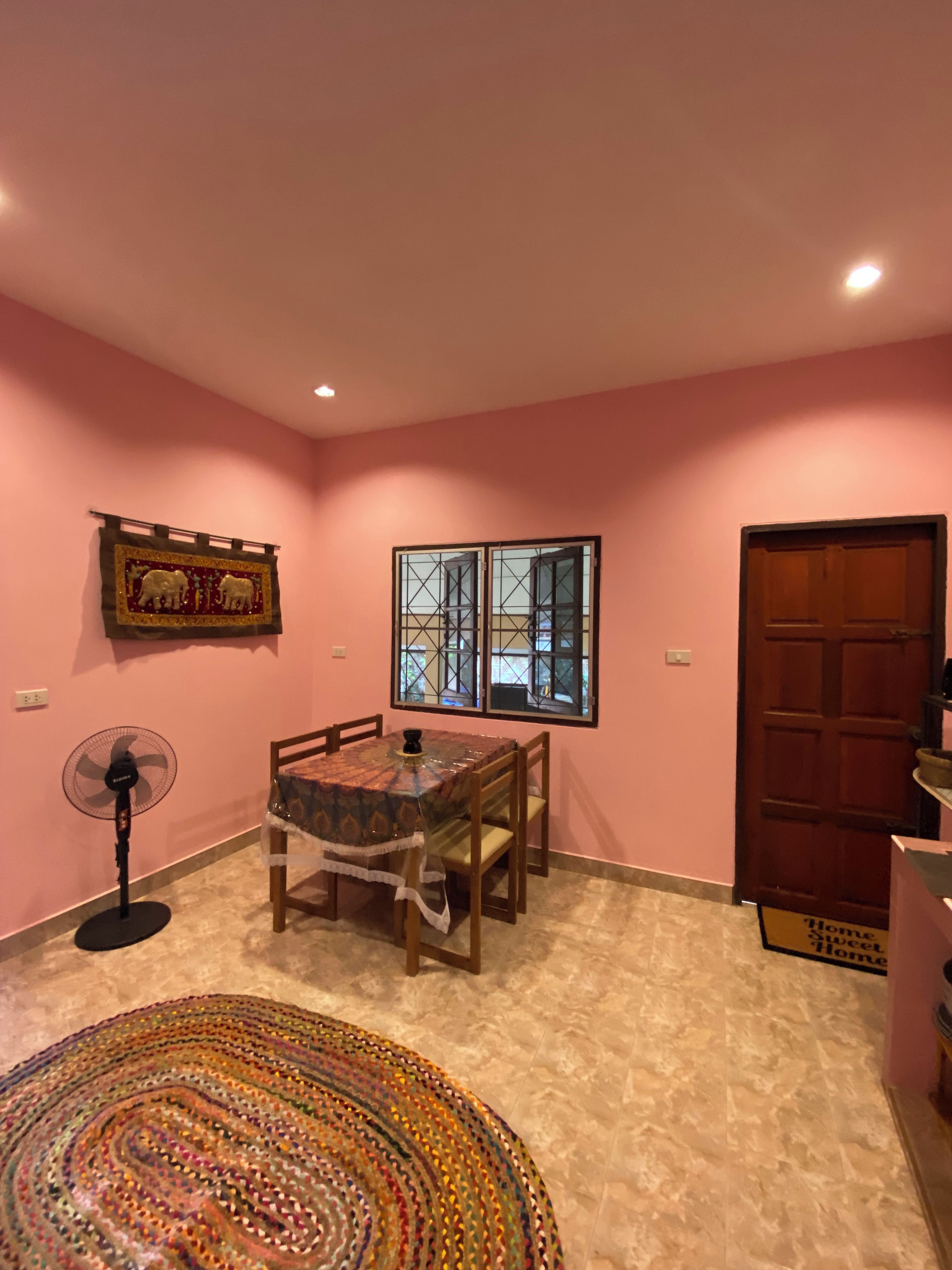 A dining area with a table, chairs, a fan, and a rug.