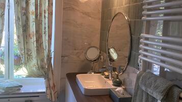 A bathroom with a sink, mirror, towel rack, and a window with curtains.