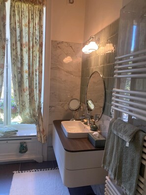 Un bagno con lavandino, specchio, portasciuga e una finestra con tende.
