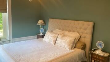 A bedroom with a large bed, a bedside table with a lamp, and a wall-mounted fan.