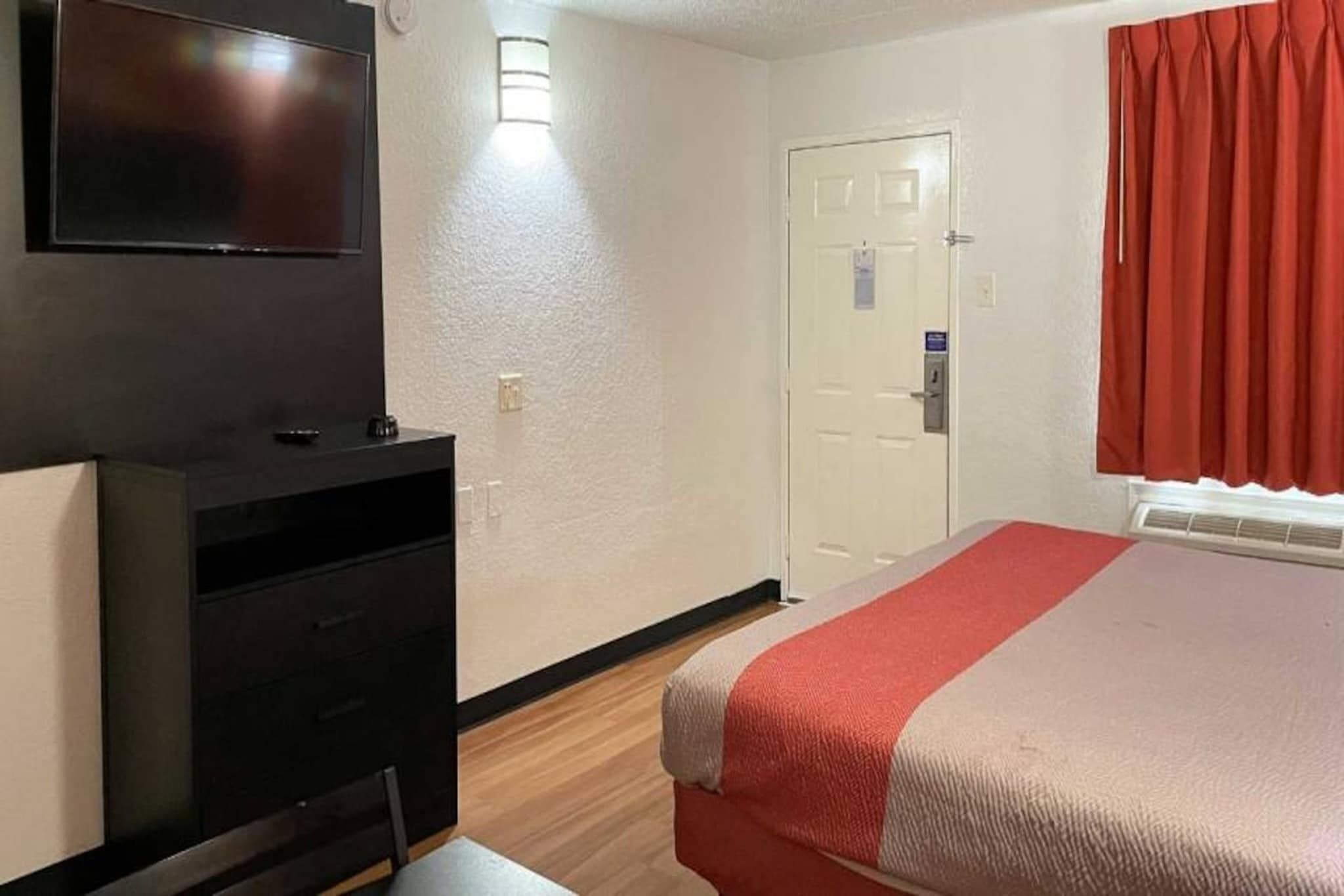 A hotel room with a bed, a TV mounted on the wall, a desk, and a door.