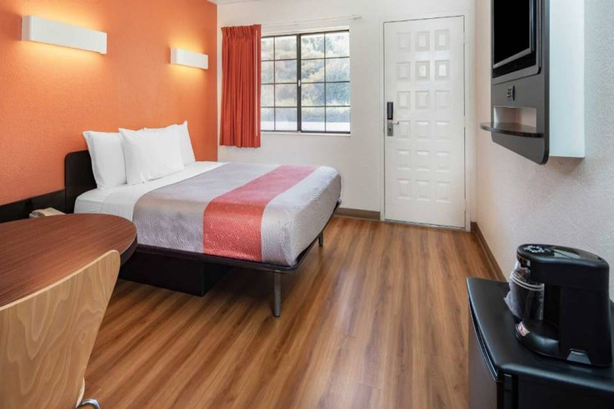 Una camera d'albergo con un letto, una scrivania, una macchina per caffè, una televisione e una finestra con tende.