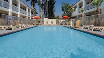 A rectangular swimming pool with lounge chairs and umbrellas on both sides, surrounded by a fence.