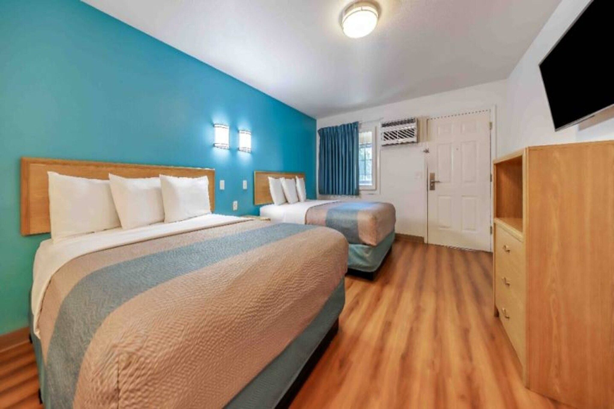 Habitación de hotel con dos camas, televisor, armario y ventana con cortinas.
