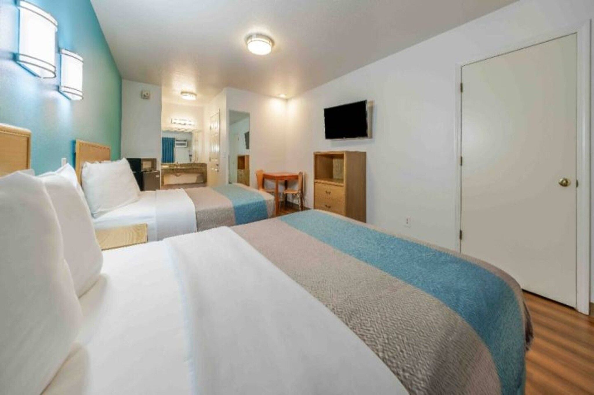A hotel room with two beds, a desk, a chair, a television, and a wardrobe.